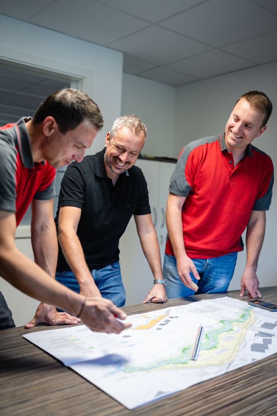 Drei Kollegen beugen sich lachend über einen Plan